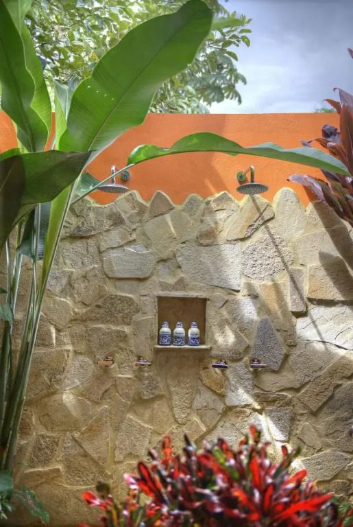 Elegante Außendusche mit Natursteinwand umgeben von tropischem Grün