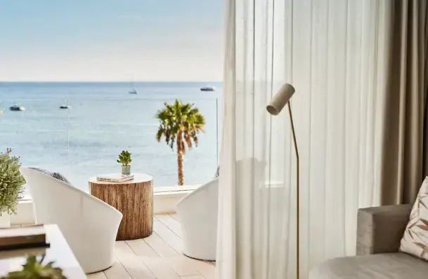 Blick auf Balkon mit Meerblick. Heller Raum mit minimalistischer Möblierung und Palmen.