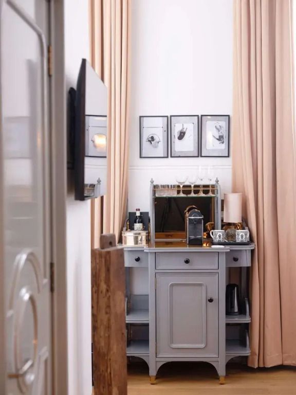Deko-Elemente und Minibar in elegantem Zimmer mit hohen Gardinen im NoMad London.