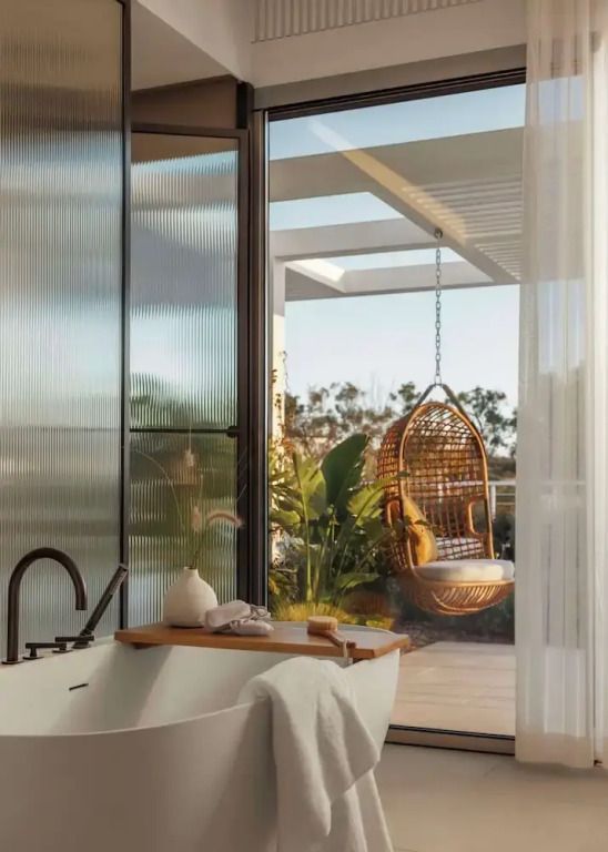 Modernes Badezimmer mit freistehender Badewanne und Zugang zu sonnigem Balkon mit Schaukelstuhl.