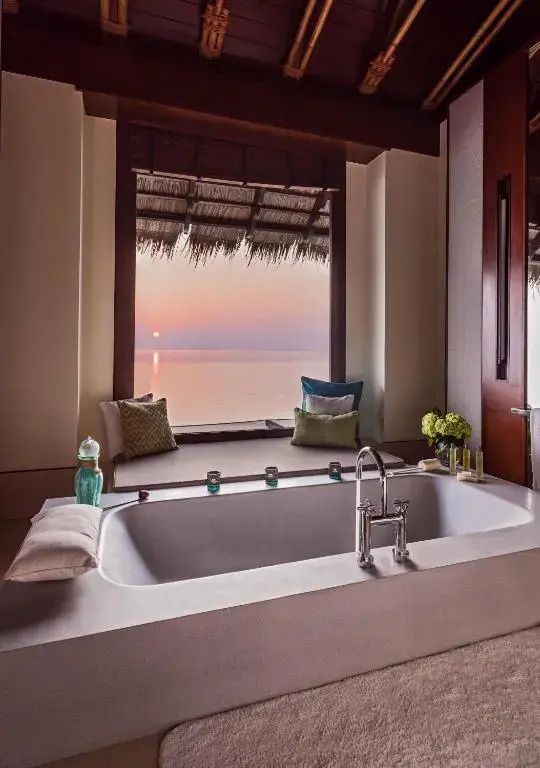 Freistehende Badewanne mit Blick auf das Meer bei Sonnenuntergang aus der Wasser-Villa.