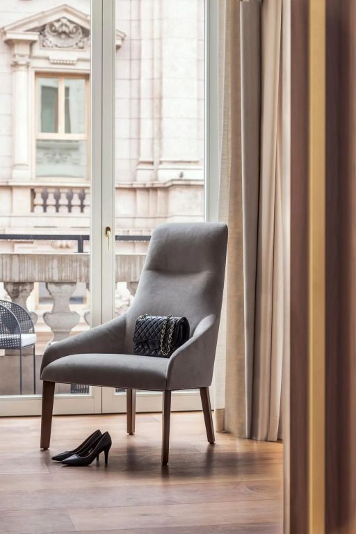 Eleganter Sessel vor großem Fenster mit Stadtblick und Balkon