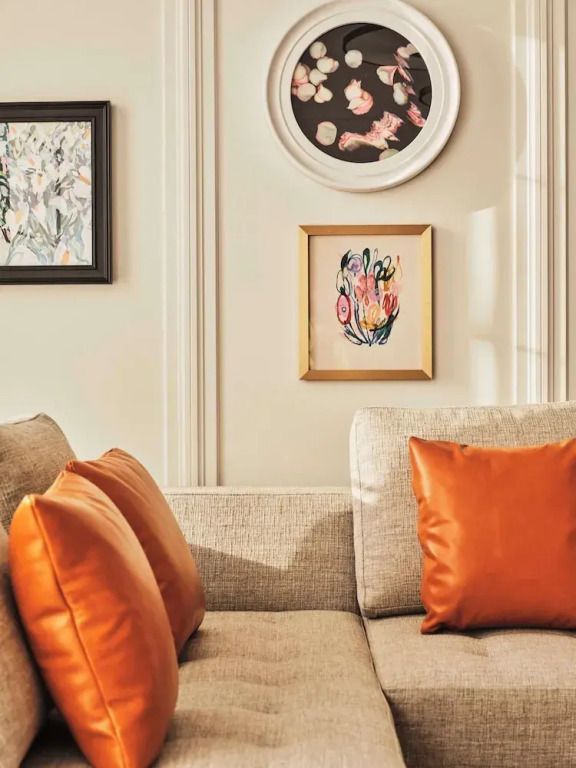 Gemütliches Sofa mit orangefarbenen Kissen und stilvollen Kunstwerken an cremefarbener Wand