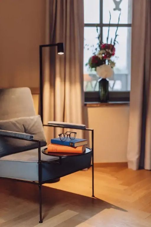 Lesesessel mit Tisch und Büchern im Zimmer mit Blumen und Vorhängen.