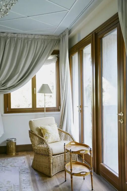 Sonniger Lesebereich mit Rattansessel und kleinen Tischchen neben großen Fenstern