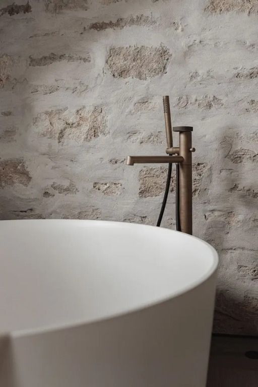 Freistehende Badewanne vor einer rustikalen Steinwand.