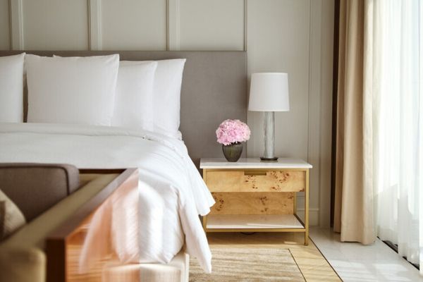 Nachttisch mit Lampe und Blumenvase, neben einem gemütlichen Doppelbett.