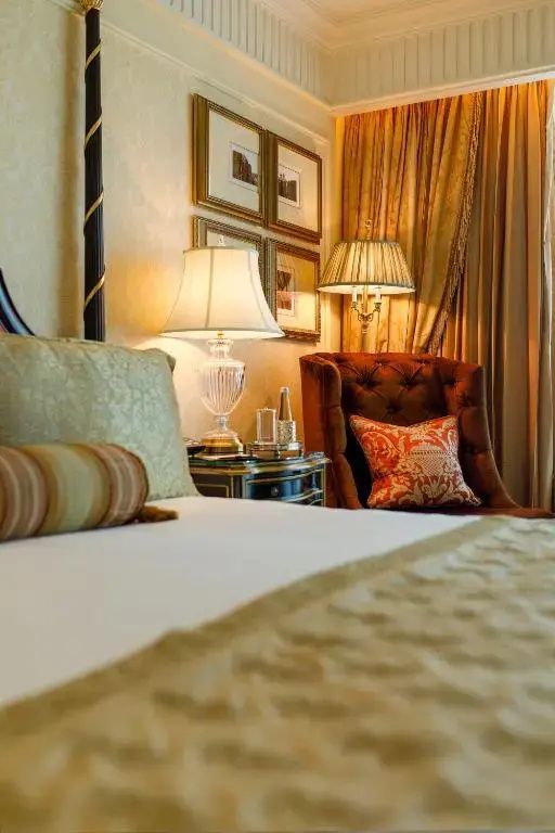 Komfortabler Sessel und elegante Bettwäsche in warmen Farbtönen im Leela Palace New Delhi