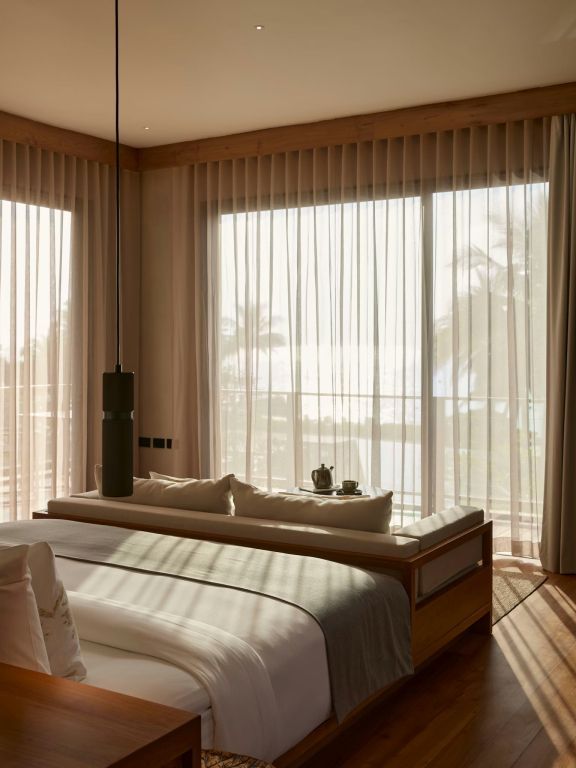 Helles Schlafzimmer mit großen Fensterfronten und Blick aufs Meer in einer Suite.