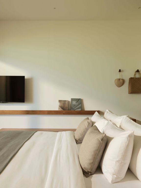 Seitlicher Blick auf gemütliches Bett mit geschmackvollen Dekorationen und Wand-TV