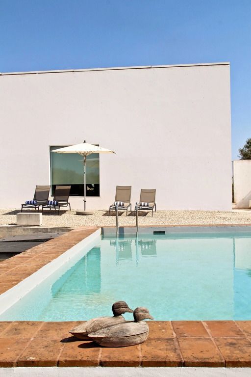 Klarer Pool mit Liegestühlen und Sonnenschirm vor minimalistischer Architektur