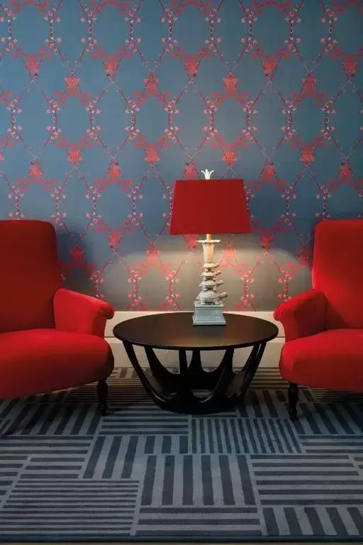 Zwei rote Sessel mit Tisch und Lampe vor gemusterter Tapete