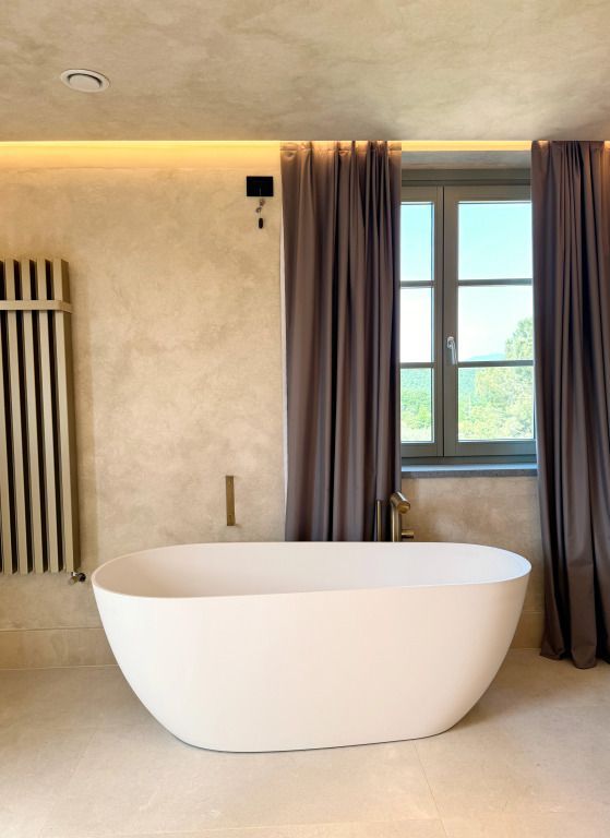 Freistehende Badewanne vor großem Fenster mit Blick ins Grüne