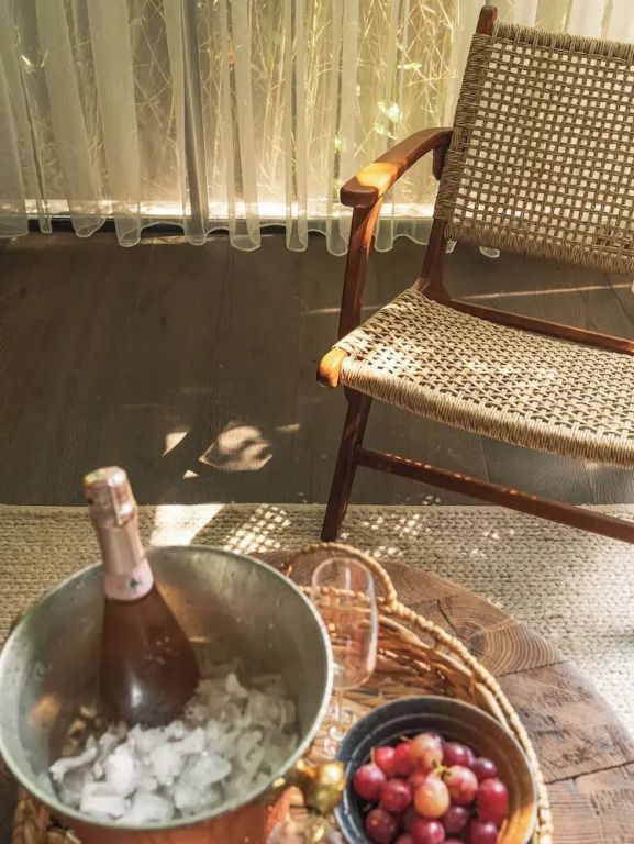Sektflasche in Eimer mit Eis auf Holztisch neben einem geflochtenen Stuhl
