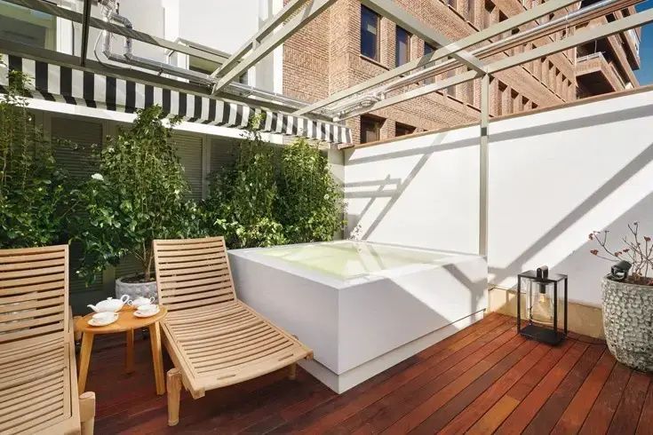 Private Holzterrasse mit Sonnenliege, Beistelltisch und weißem Whirlpool.