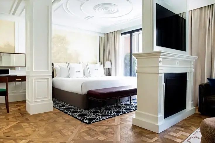 Hotelzimmer mit Doppelbett, Parkettboden und einem weißen Kamin als Raumteiler.