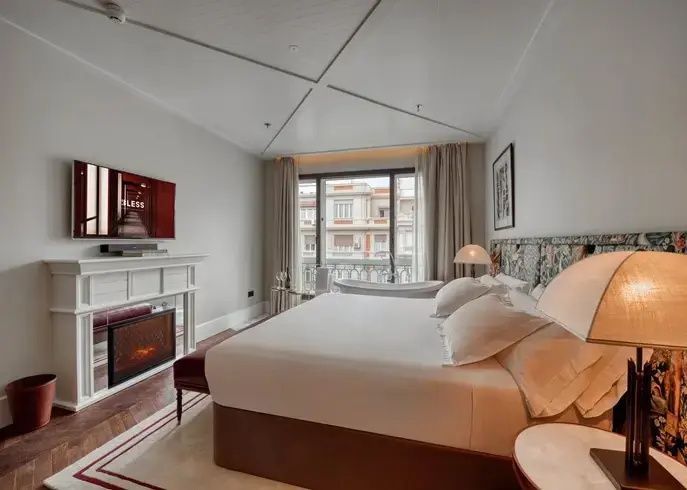 Helles Hotelzimmer mit Doppelbett, Kamin, Fernseher und freistehender Badewanne am Fenster.