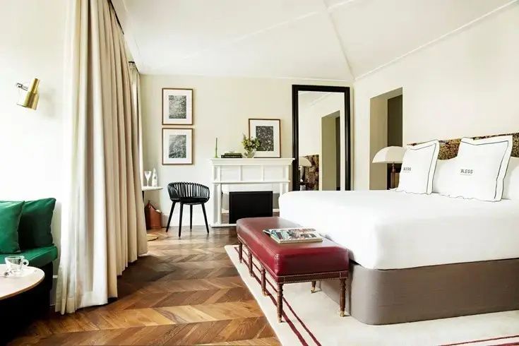 Hotelzimmer mit Parkettboden, weißem Kaminumbau, Stuhl und Doppelbett mit roter Bank.