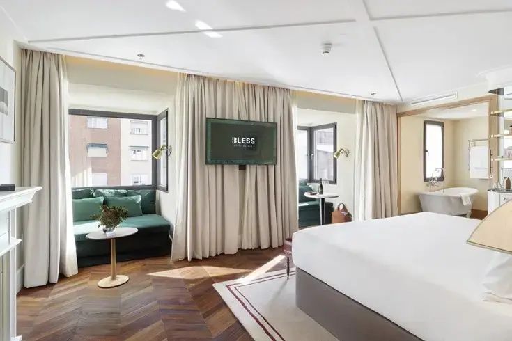 Geräumiges Hotelzimmer mit Parkett, grünem Sitzbereich am Fenster und Flachbild-TV.