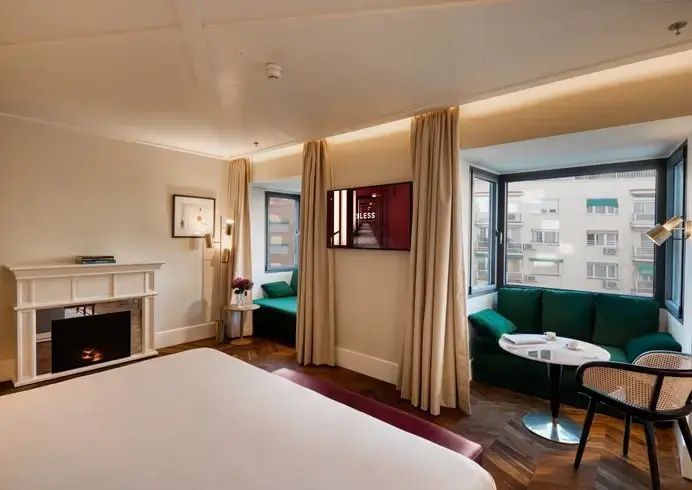 Hotelzimmer mit Kaminattrappe, grünem Ecksofa am Fenster und Fernseher an der Wand.