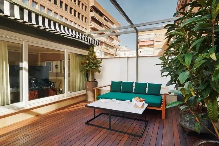 Terrasse aus Holz mit grünem Sofa, Couchtisch und Blick auf umliegende Gebäude.