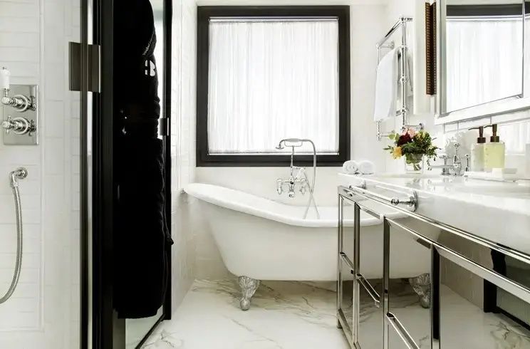 Freistehende Badewanne vor einem Fenster im Badezimmer mit Marmorboden