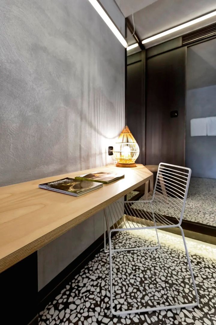 Holzschreibtisch mit weißem Metallstuhl und einer Tischleuchte auf Mosaikfußboden.
