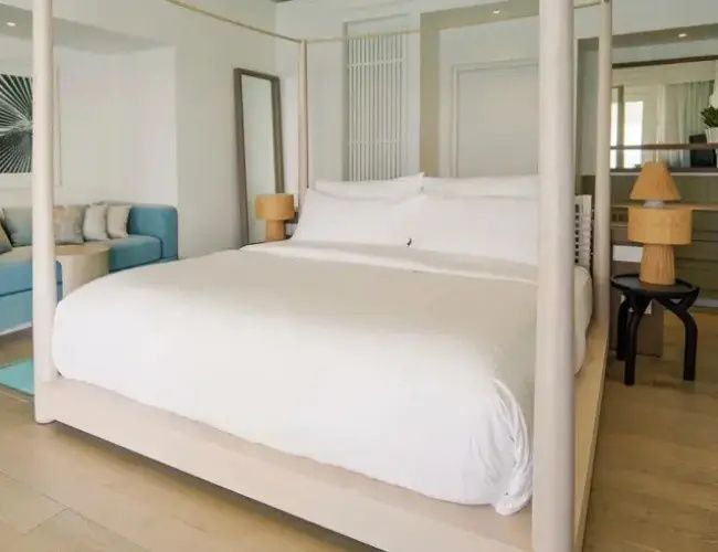 Hell eingerichtetes Hotelzimmer mit einem großen Himmelbett in Weiß, Holzfußboden und Sitzbereich.