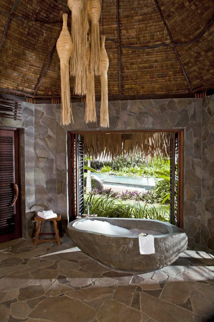 Freistehende Natursteinbadewanne mit Schaum in einem Badezimmer mit Blick ins Grüne.