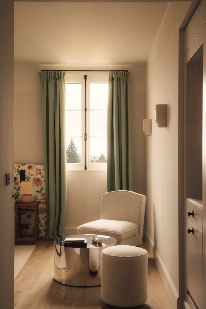 Helles Hotelzimmer mit einem Sessel, grünen Vorhängen und einem Fenster mit Blick nach draußen.