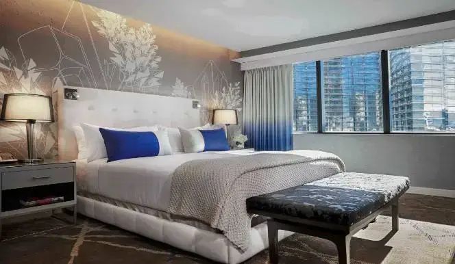 Doppelbett mit weißer Bettwäsche, blauen Kissen und Wanddekoration neben einem Fenster.