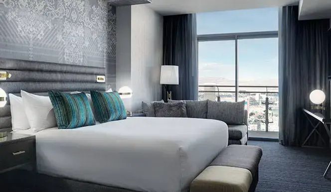 Modernes Hotelzimmer mit großem Doppelbett, Sofa und Fensterfront mit Blick auf die Stadt.