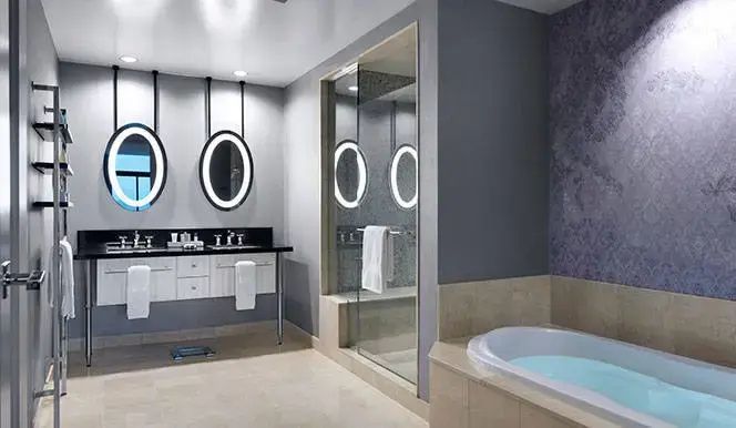 Badezimmer mit doppeltem Waschtisch, ovalen beleuchteten Spiegeln, Dusche und Badewanne.
