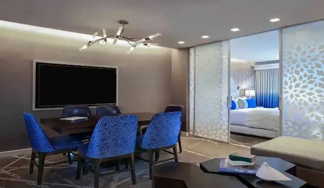 Esstisch mit blauen Stühlen und Couchtisch in einem Suite-Wohnbereich vor Schiebetür.