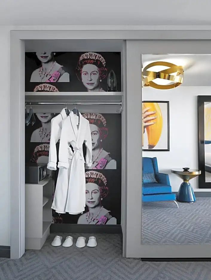 Offener Kleiderschrank im Hotelzimmer mit weißem Bademantel und gemusterter Tapete.