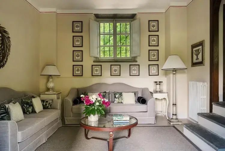 Wohnbereich mit grauem Sofa, Glascouchtisch mit Blumen und eingerahmten Bildern an der Wand.