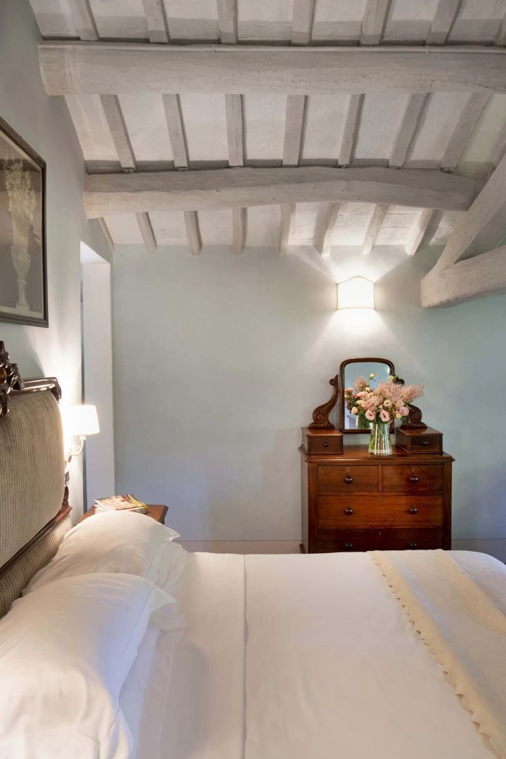 Helles Zimmer mit Doppelbett, beigen Holzbalken an der Decke und einer braunen Holzkommode.