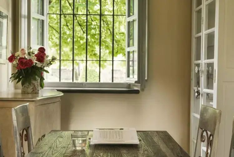 Holztisch mit aufgeschlagenem Buch und Wasserglas vor einem Fenster mit Gitterstäben.