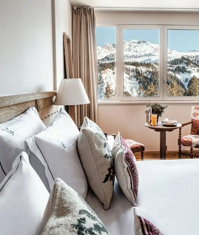 Bett mit Bergen durch Fenster im Hintergrund und Tisch mit Getränken