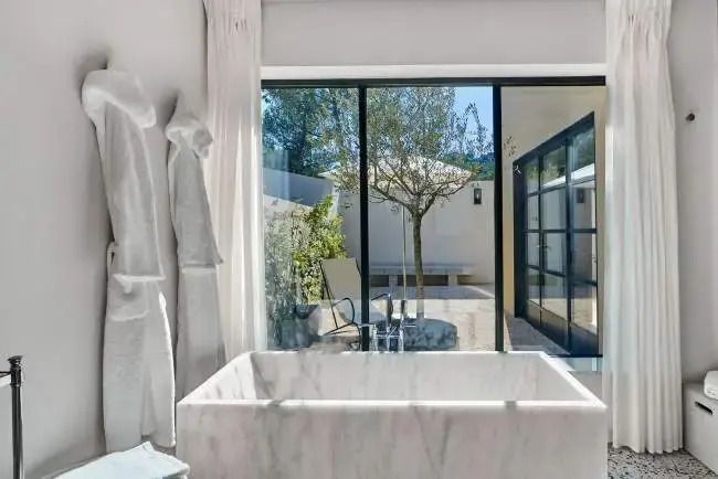 Luxuriöses Badezimmer mit freistehender Badewanne und Blick auf Gartenterrasse
