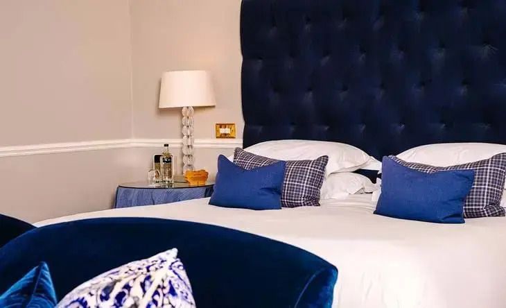 Elegantes Schlafzimmer mit blauem Kopfteil und dekorativen Kissen im Croquet Lawn Doppelzimmer.