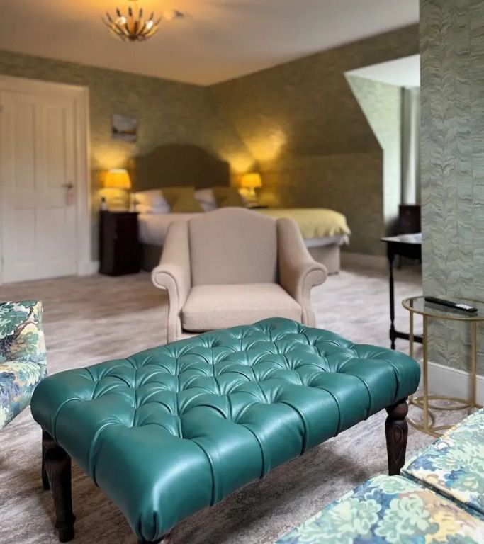 Lounge-Bereich mit grüner Ledercouch, Sessel und Sicht auf ein Bett