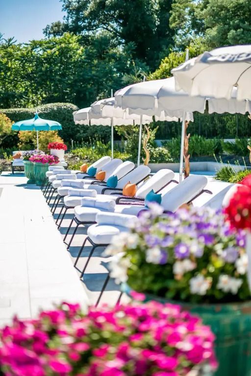 Sonnenliegen am Pool mit Sonnenschirmen und blühenden Blumen im Garten.