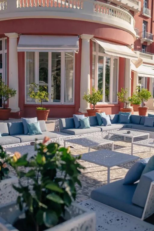 Elegante Außenterrasse mit blauen Sofas und Pflanzen vor dem Gebäude.
