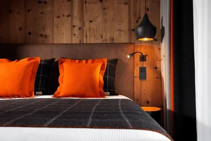 Detailansicht eines Doppelbetts mit orangefarbenen Kissen vor holzgetäfelter Wand.