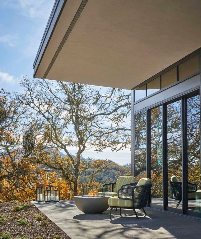 Terrasse mit modernen Möbeln und Feuerstelle, umgeben von Eichen und Blick in die Natur