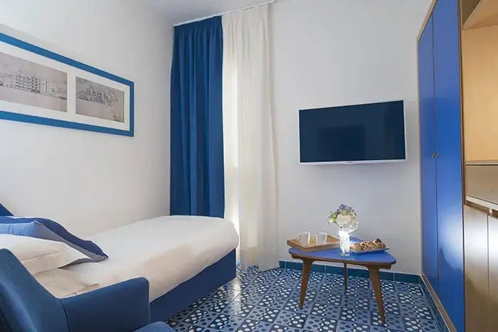 Gemütliches Zimmer mit Einzelbett und Flachbildfernseher in blau-weißen Tönen.