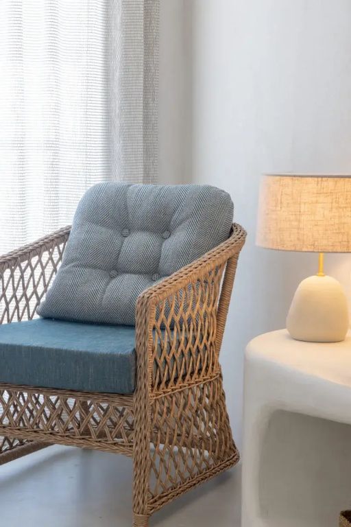 Eleganter Rattan-Sessel mit blauem Polster und moderner Tischleuchte im Hotelzimmer.