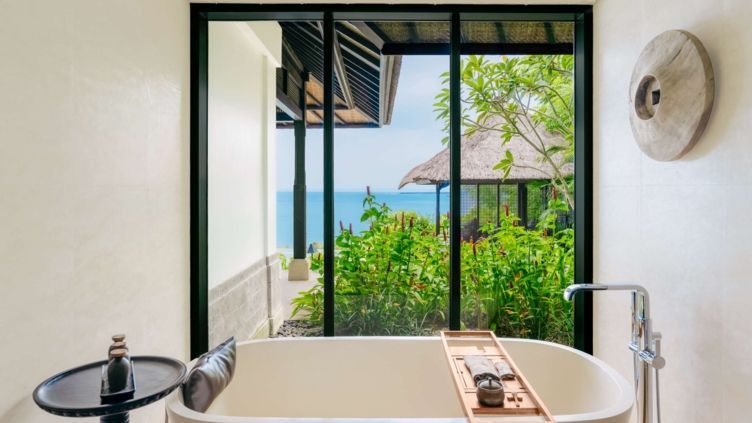Badezimmer mit freistehender Badewanne und Ausblick auf das Meer und Garten