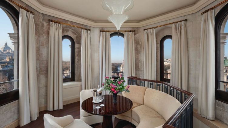Turmzimmer mit Panoramafenstern, runder Sofaecke und frischen Blumen.